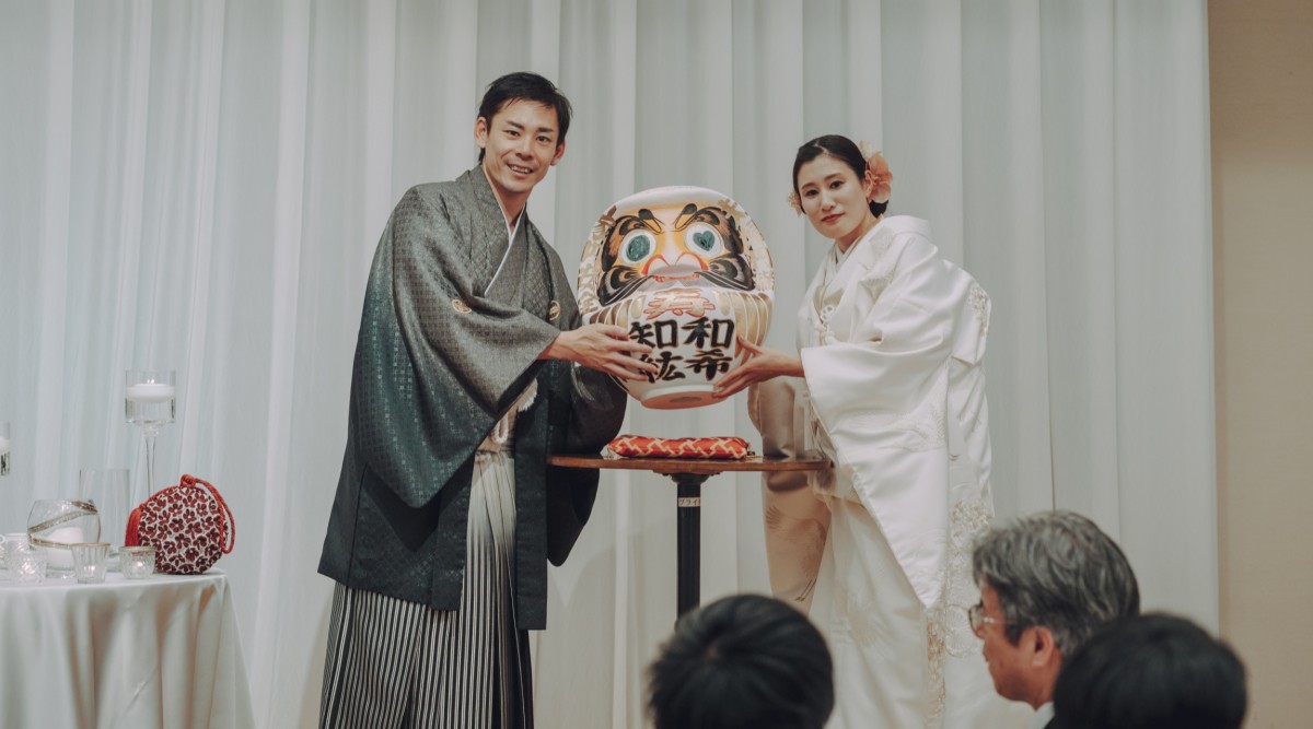 和装新郎新婦がだるまを持っている